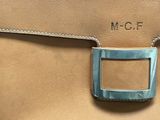 the back of a brown purse with a metal buckle on it