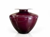 un vase violet avec un couvercle argenté posé sur une surface blanche