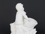 a white figurine of a woman sitting on top of a basket