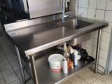 a stainless steel table with a sink and a refrigerator in the background