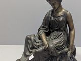 bronze statue of a woman sitting on a rock with a bird in her hand