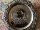 une assiette en argent ornée d'un oiseau, posée sur une nappe à motifs floraux