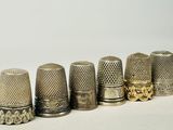 six antique thimbles lined up in a row on a white surface
