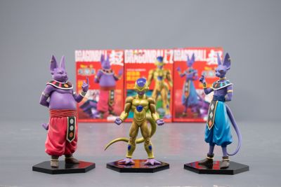 trois figurines représentant des personnages de Dragon Ball exposées devant une boîte remplie de livres