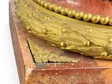 a gold and red clock on a marble base