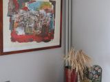 a red vase sitting on a wooden shelf next to a painting