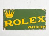 une enseigne représentant une montre Rolex verte et jaune sur un mur blanc