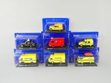 six petites voitures miniatures dans des boîtes en plastique, posées sur une surface blanche