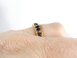 a woman ' s hand holding a gold ring with black stones