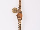 an image of a gold watch with a leaf charm on it