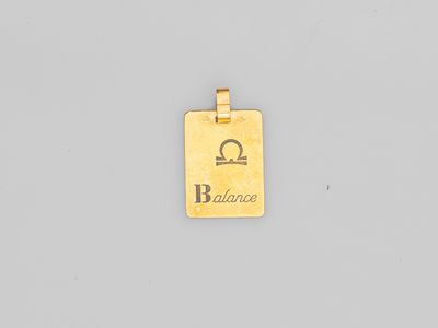 une image d'un pendentif plaqué or sur lequel figure le mot « balance »