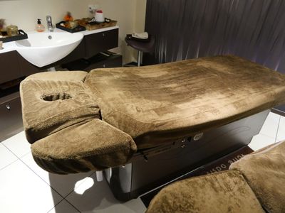 une table de massage au milieu d'une pièce, avec un lavabo en arrière-plan