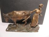 bronze statue of a woman pulling a cart with a cow