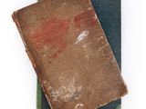 two old books are stacked on top of each other on a white surface