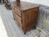 une commode en bois sur laquelle est posé un vase, près d'un mur