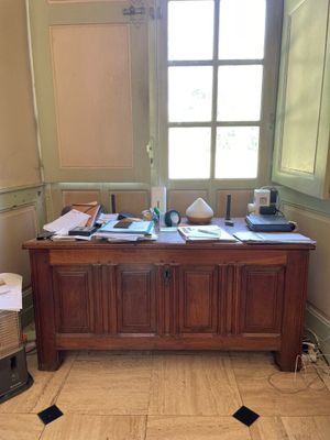un bureau dans une pièce dotée d'une fenêtre, sur lequel sont empilés de nombreux papiers