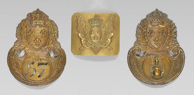 trois plaques en laiton représentant une couronne, un blason et un autre blason sur fond blanc
