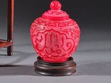 un vase rouge posé à côté d'une chaise sur une surface grise
