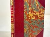 an old book with a red cover and gold trim on a white surface