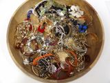 a wooden bowl filled with assorted jewelry on a white surface