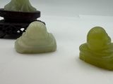 four jade buddha figurines sitting on a white surface next to a vase