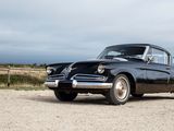 an old black car parked in a gravel lot
