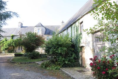 une allée menant à un bâtiment en pierre devant lequel se trouve un rosier rouge
