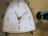une horloge blanche posée sur une table en verre, avec une bouteille de vin en arrière-plan