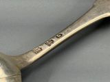une cuillère en argent avec un manche en métal posée sur une table