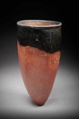 un vase orange et noir posé sur une table blanche