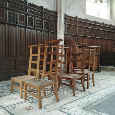 Plusieurs chaises en bois sont alignées dans une pièce dont un mur est recouvert de lambris.