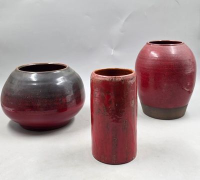 trois vases rouges et noirs posés les uns à côté des autres sur une surface blanche