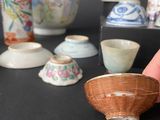 a person that is holding a small bowl in front of a collection of vases