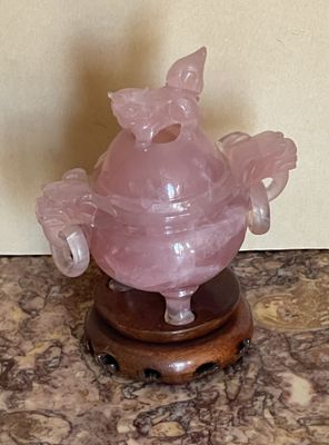 un vase rose posé sur un socle en bois, lui-même posé sur une surface en marbre