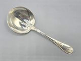 une cuillère ancienne en argent avec un manche, posée sur une surface blanche