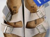 Deux paires de Birkenstock sont présentées sur une surface blanche.