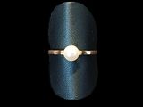 un gros plan d'une bague sertie d'une perle, posée sur une surface noire