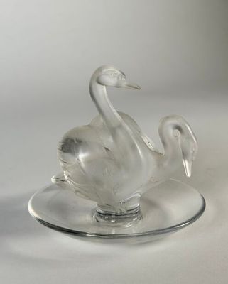 a glass swan on a plate on a white surface