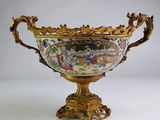 un grand vase décoré, posé sur un socle doré, avec un fond blanc
