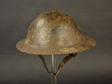 un vieux casque militaire posé sur un socle, sur fond gris