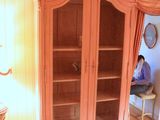 a pink cabinet in the corner of a room with floral wallpaper