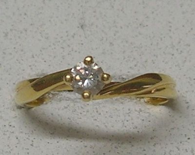 une bague en diamant posée sur une surface blanche, avec un anneau en or