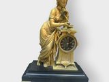 a gold statue of a woman with a clock on a table