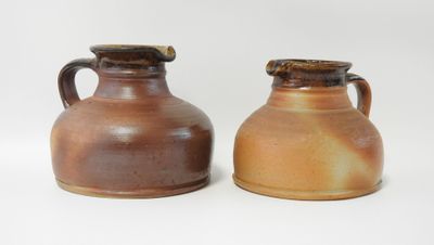 deux vases marron munis d'anses, posés côte à côte sur une surface blanche