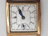 une petite montre carrée en or avec une trotteuse bleue