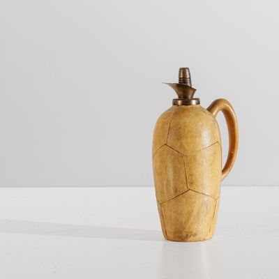 une vieille cruche en bois avec un couvercle en métal, posée sur une surface blanche