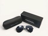 Des lunettes de soleil Chanel dans un coffret noir et un étui, posés sur une surface blanche