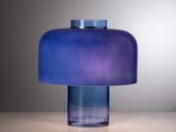 une lampe de table en verre bleu posée sur une table blanche