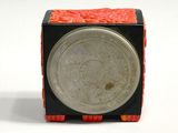 a small black and red box with a silver coin on it
