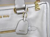 a white purse with a gold handle and a name tag on it
